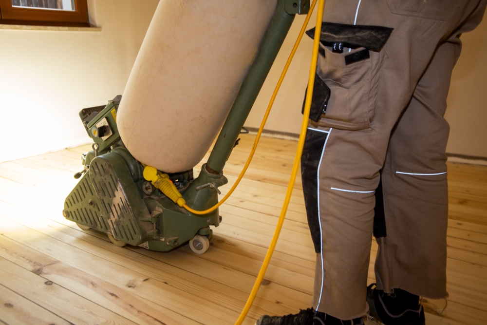 A professional operating a floor sanding machine on unfinished wooden boards, illustrating Wood Floor Sanding in progress.