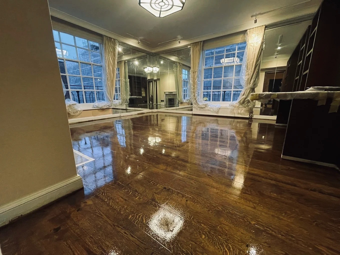 Commercial Floor Sanding in Kent – high-gloss dark oak hardwood plank floor in an elegant commercial room with large windows and mirrors after full restoration.