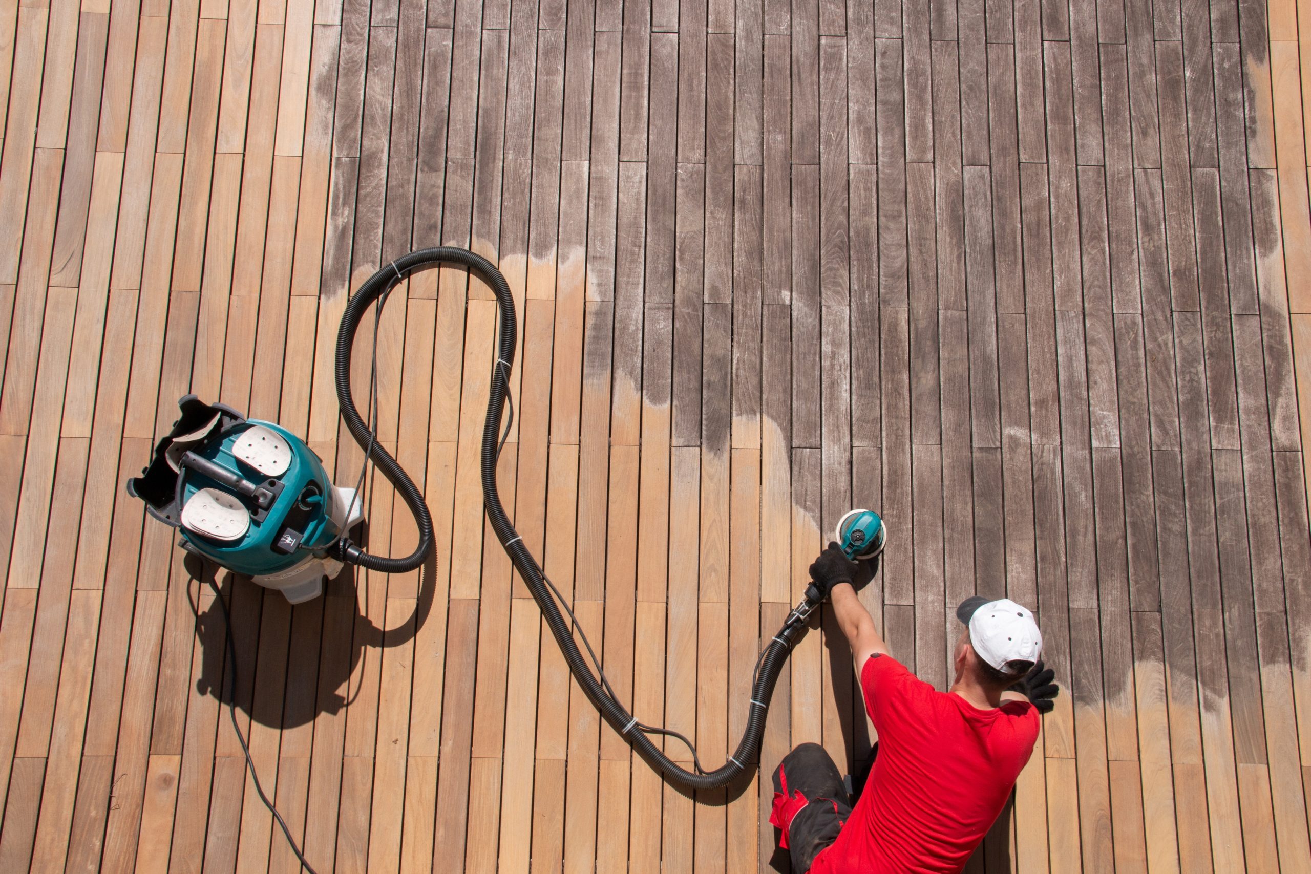 Commercial Floor Sanding in Kent – technician sanding weathered hardwood timber deck boards with a dust-extraction sander to restore the exterior deck floor.