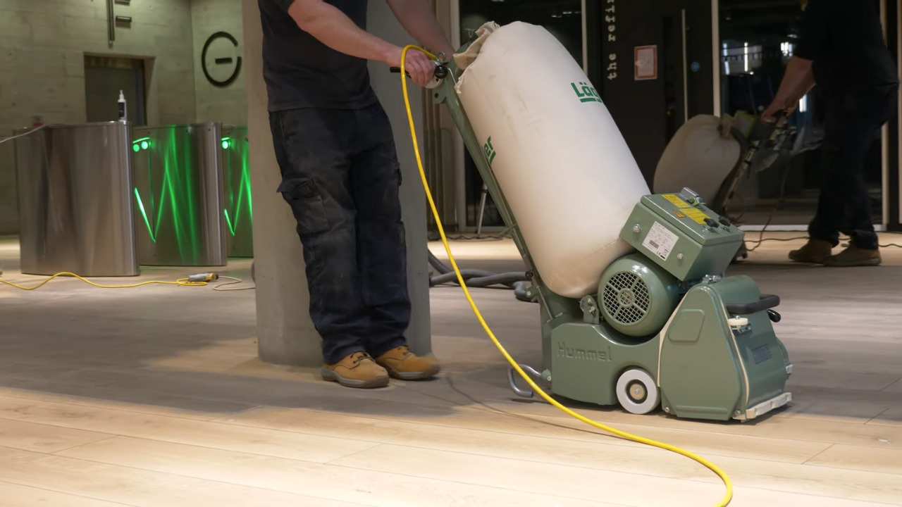 Commercial Floor Sanding in Kent – technician using a Lagler Hummel belt sander on a light oak hardwood plank reception floor in a modern commercial building.
