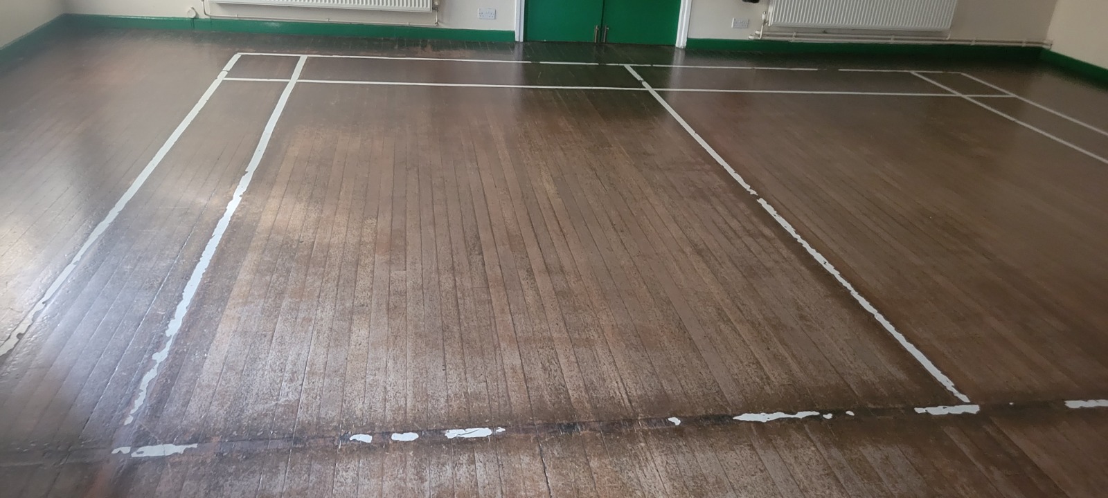 Commercial Floor Sanding in Kent – dark, worn maple strip hardwood sports hall floor with faded court lines before sanding and restoration.
