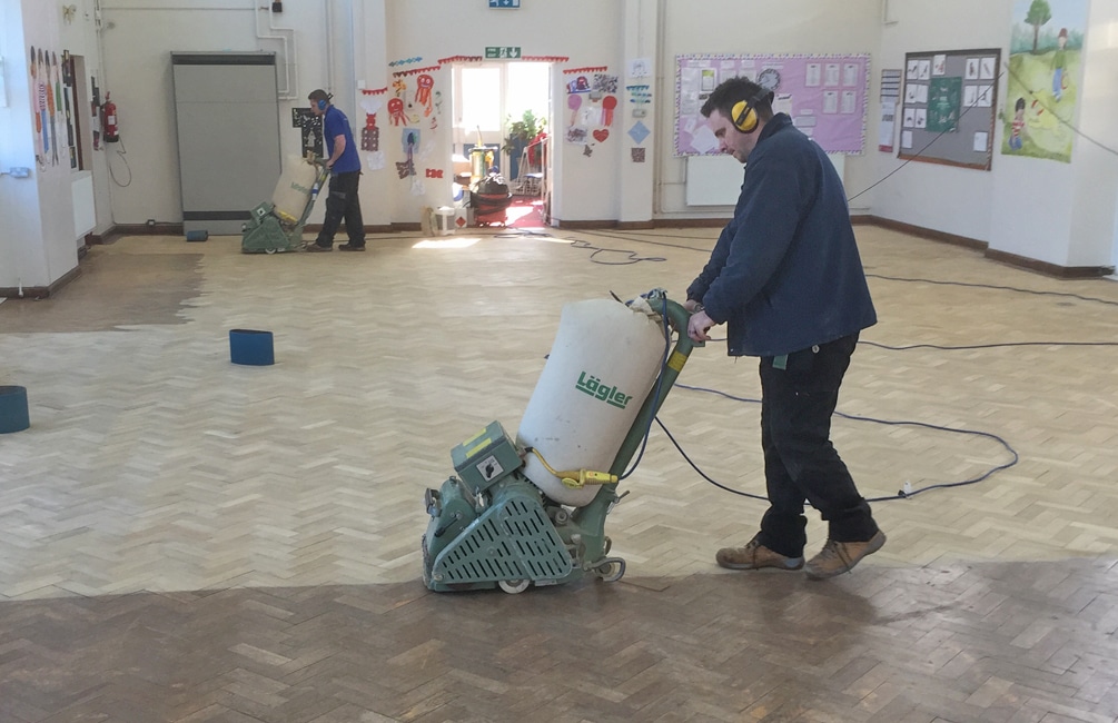 Commercial Floor Sanding in Kent – team sanding an oak herringbone parquet school hall floor with professional Lagler machines during restoration.
