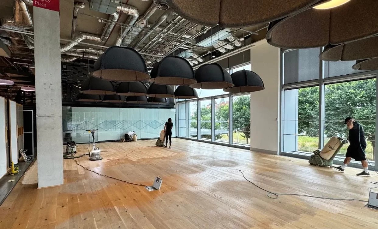Commercial Floor Sanding in Kent – contractors sanding and restoring an oak wide plank hardwood office floor in a modern open-plan workspace with large windows.