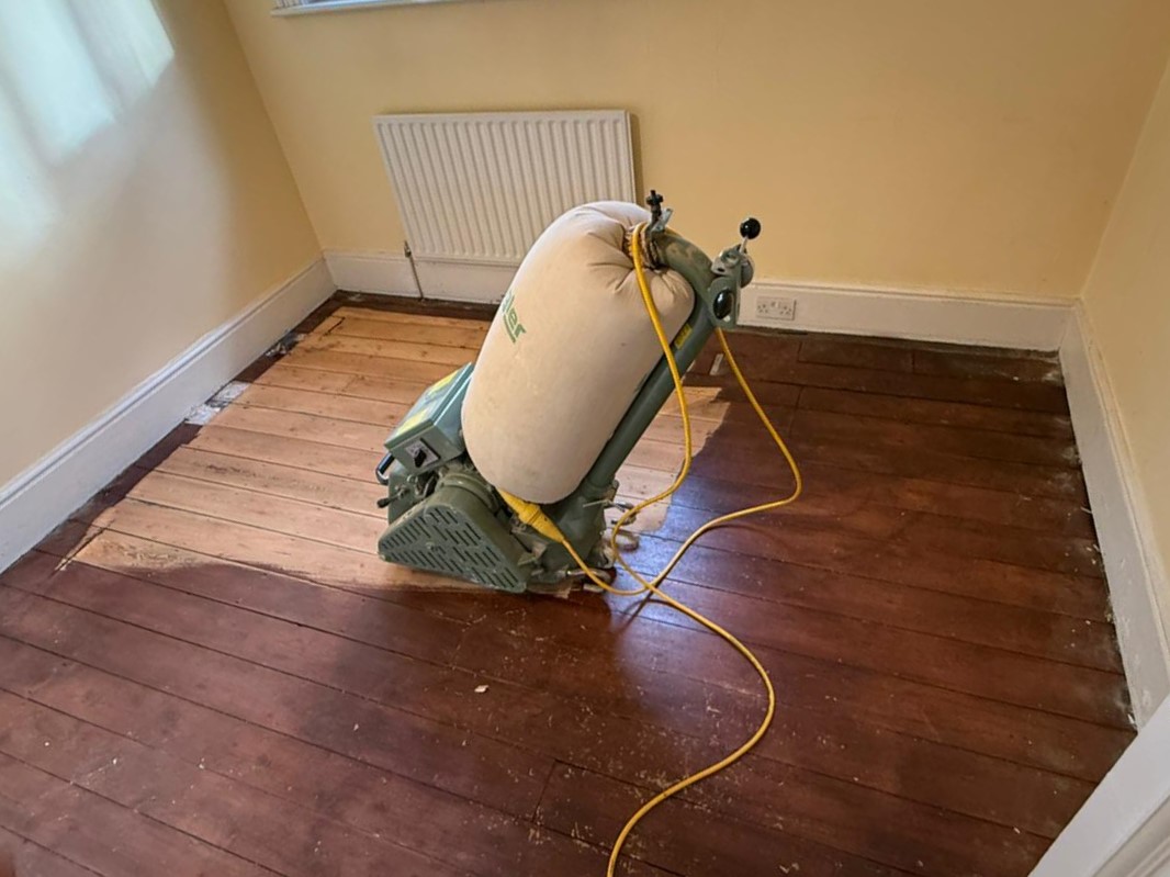 Wood Floor Sanding in Kent on original solid pine floorboards, showing a drum sander stripping dark stain to reveal fresh pale timber.