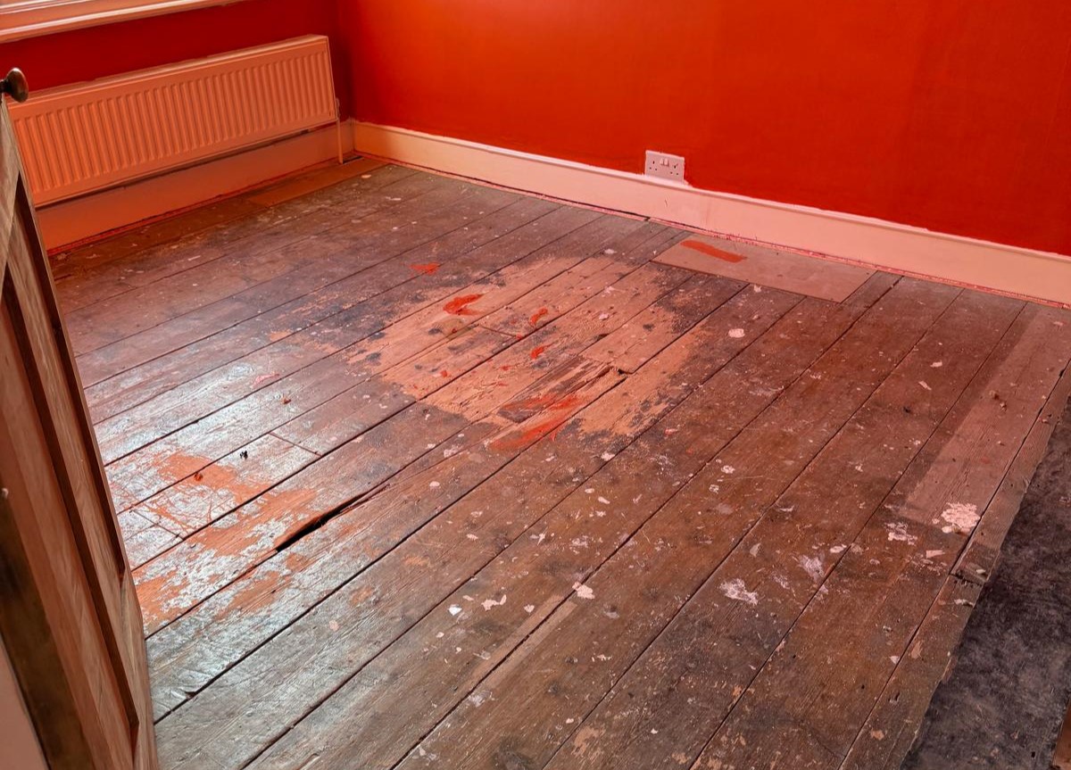 Wood Floor Sanding in Kent on worn solid pine floorboards in a bedroom, showing dark, paint-splattered boards before restoration.